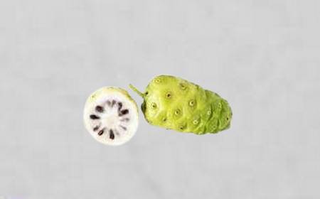 Un noni entier avec sa texture bosselée, de couleur vert-blanc